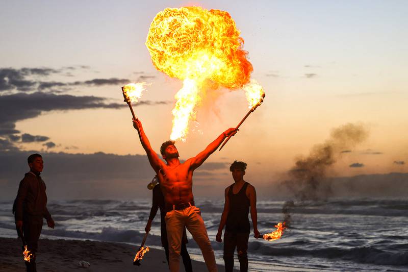 A Palestinian performer in Gaza city blows a cloud of flame on the beach, where spectators gather and sand serves as a damper of flames.