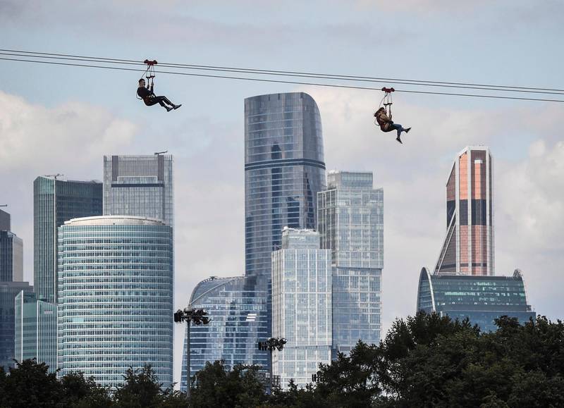 People slide along a zipline over the Moskva river from Vorobyovy Hills observation point to the Luzhniki Olympic stadium in front of the towers of Moscow's International Business Centre (Moskva City) in Moscow on August 20, 2020. The Federation Tower on the centre. (Photo by Alexander NEMENOV / AFP)