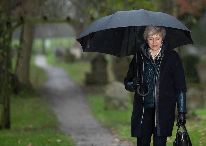 Britain's Prime Minister Theresa May shelters from the rain under an umbrella after attending a church service near to her Maidenhead constituency, west of London on December 9, 2018. Theresa May wants to go down in history as the prime minister who safely steered Britain out of Europe -- a cause she did not believe in when the Brexit referendum was held. / AFP / Daniel LEAL-OLIVAS
