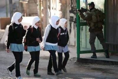 An Israeli border policeman aims his weapon as Palestinians school girls walk near a building occupied by Israeli settlers in the West Bank city of Hebron on Tuesday.