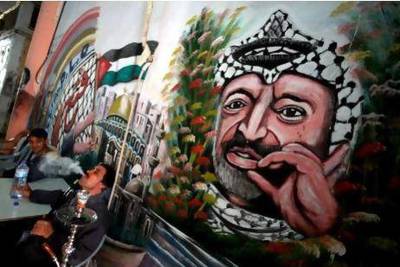 Palestinian men sit in a cafe near a mural of their late leader Yasser Arafat in the West Bank city of Jenin. Arafat’s wife Suha alleges he was poisoned before his 2004 death.