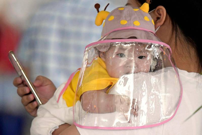 A baby with a face shield waits to board a plane at an airport in Wuhan, central China's Hubei Province. Kyodo News via AP