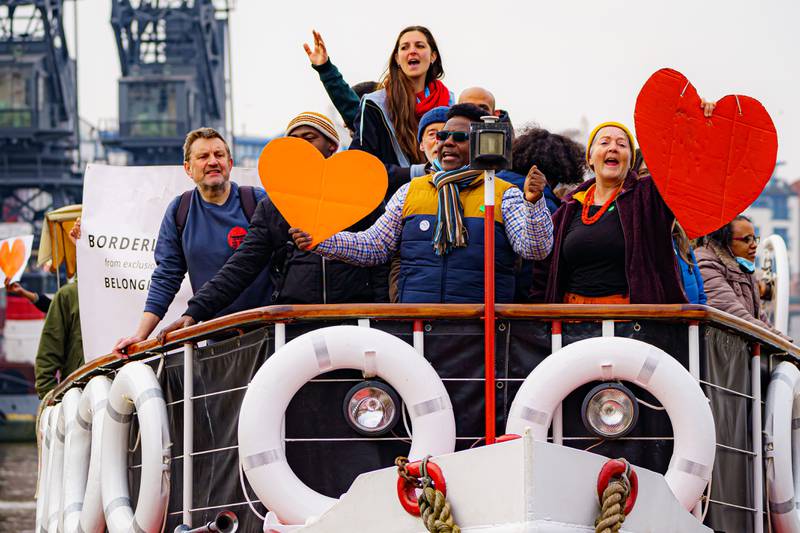 People wave banners and cardboard cut-out hearts aboard a small flotilla of boats leaving Bristol on Monday in support of Ukrainian refugees. PA