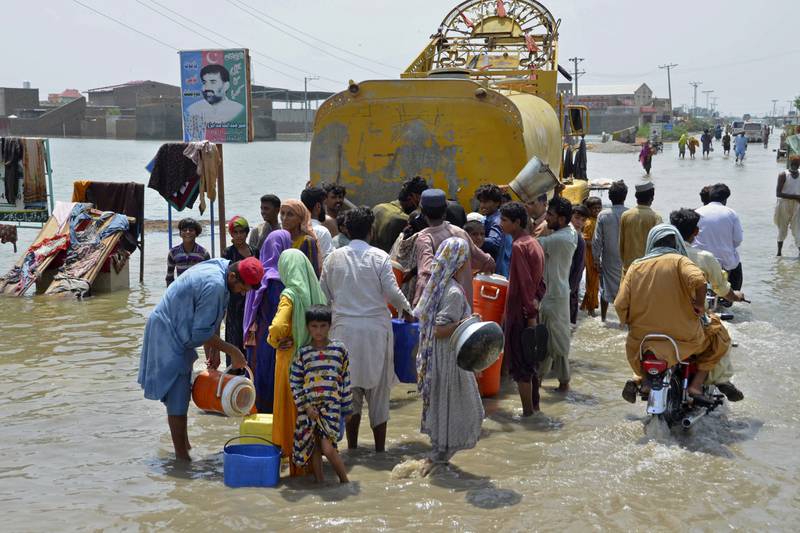 People jostle for drinking water delivered by a municipality lorry along a flooded road in Sohbatpur, Balochistan. AP