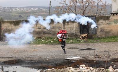 A Palestinian medic seeks cover from a tear gas grenade fired by Israeli troops during clashes after a demonstration against Israel's settlements in the village of Kofr Qadom, near the northern West Bank city of Nablus. EPA