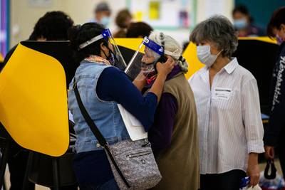 A woman helps an elderly voter put on headphone to follow directions as she casts her ballot at the Salazar Park polling location in Los Angeles, California.  EPA