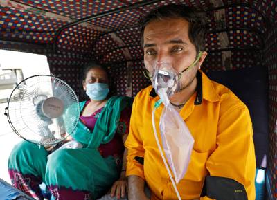 A patient wearing an oxygen mask looks on as his wife holds a battery-operated fan as they wait inside an auto-rickshaw to enter a Covid-19 hospital, in western Indian city of Ahmedabad. Reuters