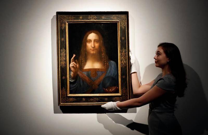 FILE- In this Oct. 24, 2017 file photo, an employee poses with Leonardo da Vinci's "Salvator Mundi" on display at Christie's auction rooms in London. The rare painting of Christ, which that sold for a record $450 million, is heading to a museum in Abu Dhabi. The newly-opened Louvre Abu Dhabi made the announcement in a tweet on Wednesday, Dec. 6. (AP Photo/Kirsty Wigglesworth, File)
