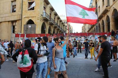 epa08595570 Protesters wave a Lebanese flag during protests near the parliament in Beirut, Lebanon, 10 August 2020. According to reports, anti-government protests continued in Lebanon despite the resignation of three ministers and several members of the parliament, as protesters are demanding the resignation of the government and all those responsible for the port explosion be held accountable. Beirut governor said at least 200 people were killed in the explosion on 04 August and dozens are still missing.  EPA/NABIL MOUNZER