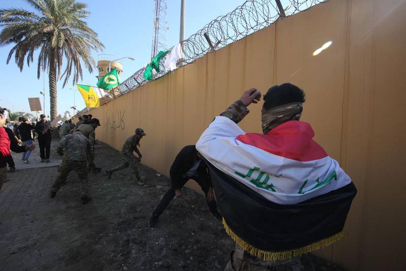An Iraqi protester draped in a national flag and members of the Popular Mobilisation Forces paramilitary group are pictured in front of the outer wall of the US embassy in Baghdad during a demonstration to denounce weekend US air strikes that killed Iran-backed fighters in Iraq. AFP