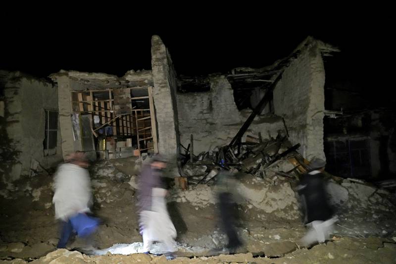 Afghans walk by a destroyed house in the village of Gyan. AP