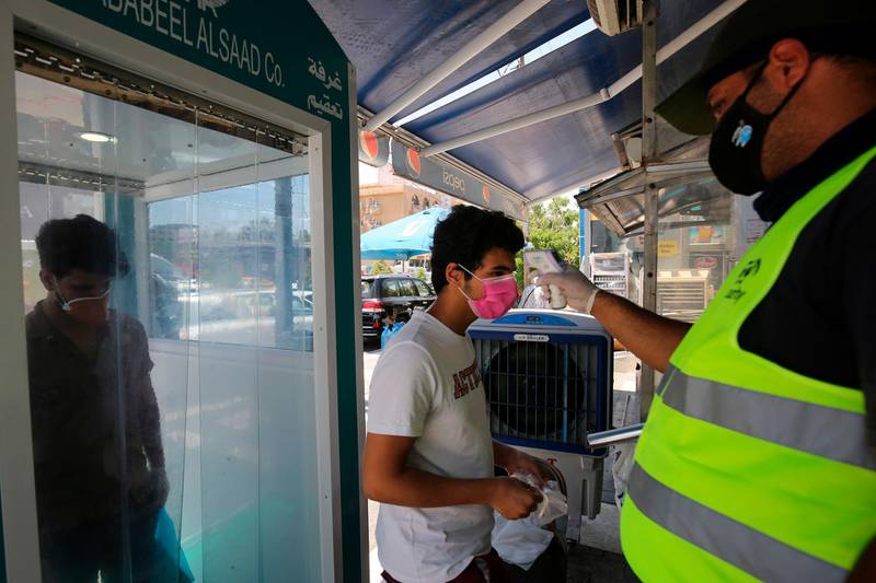 A customer, wearing a protective mask, gets his temperature checked after passing through an automatic disinfection booth at the entrance of a supermarket in the Iraqi capital Baghdad.   AFP