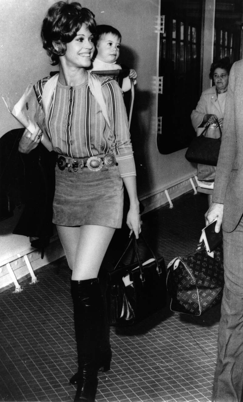 Jane Fonda, in a denim mini-skirt and striped shirt, carrying her baby daughter on arrival at Le Havre, France, on June 5, 1969