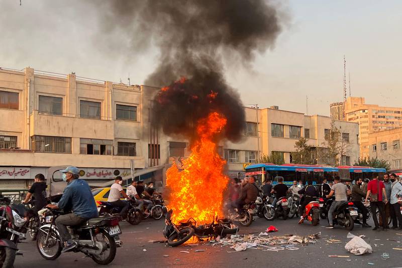 People gather next to a burning motorcycle.