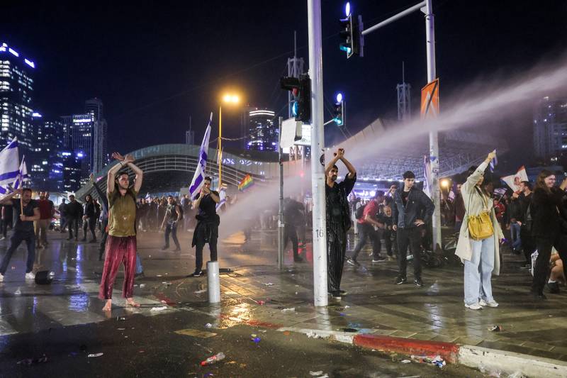 Protesters stand with their arms up as police fire a water cannon in Tel Aviv. Reuters