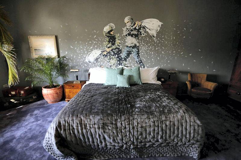 epa05829120 An artwork, depicting an Israeli soldier (L) and a Palestinian protester during a pillow fight, by British street artist Banksy is painted onto a wall in a bedroom of the Walled Off Hotel in the West Bank city of Bethlehem, 04 March 2017. The hotel in the Palestinian territories is placed only a couple of meters from Israel's separation wall with all rooms facing it. The Walled Off Hotel will open for guests on 20 March, with bookings via the website.  EPA/ABED AL HASHLAMOUN *** Local Caption *** 53368007
