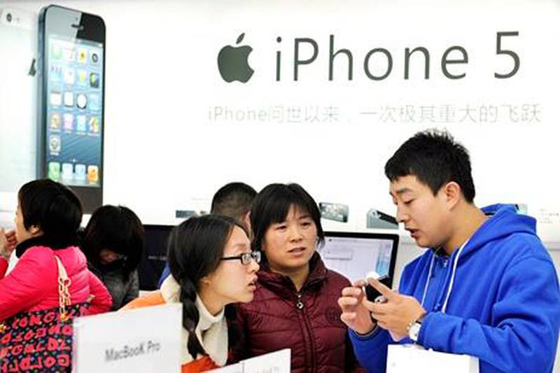 A storekeeper introduces iPhones to customers near an iPhone 5 advertisement at an Apple products shop in Dongyang, in eastern China's Zhejiang province, Friday, Dec. 14, 2012. Apple released the latest version of its smartphone in China on Friday. (AP Photo)  CHINA OUT *** Local Caption ***  China Apple iPhone 5.JPEG-08ef4.jpg