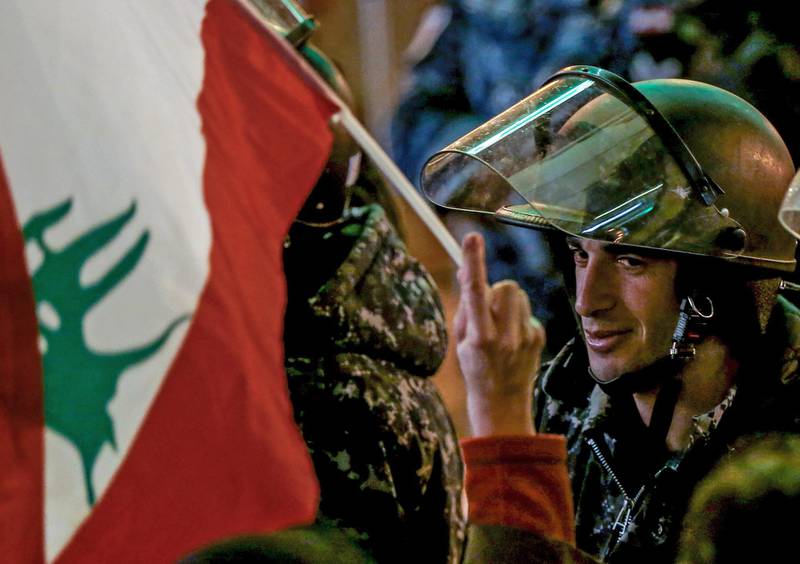A protester waves the Lebanese flags in front of Lebanese policemen at a barricade, during an anti-government protest in front of the Parliament building in Beirut on Sunday, December 8. EPA