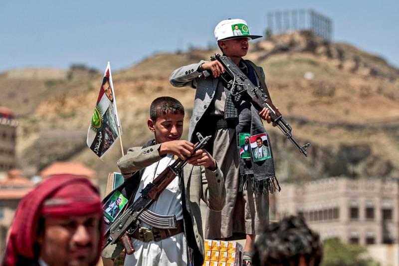 A Yemeni boy lines up a round of ammunition atop the barrel of a Kalashnikov assault rifle, with a flag sticking from his jacket showing a picture of the Huthi rebel leader Abdulmalik al-Huthi, while another buy stands with Kalashnikov over a crate of juice boxes during a tribal meeting in the Huthi rebel-held capital Sanaa on September 21, 2019, as tribesmen donate rations and funds to fighters loyal to the Huthis along the fronts. (Photo by MOHAMMED HUWAIS / AFP)
