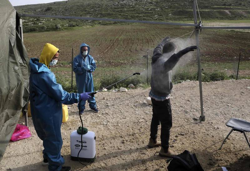 An employee at the Palestinian ministry of health sprays disinfectant on a worker returning from Israel through the Tarqumiah crossing, north-west of the West Bank city Hebron to stem the spread of the COVID-19 pandemic.  AFP