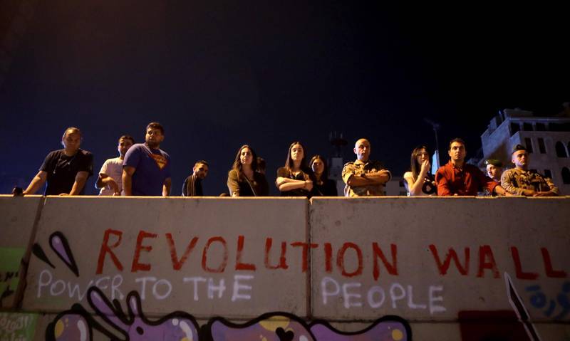 Lebanese anti-government protesters and a Lebanese army soldier (R) stand behind a wall reading "Revolution Wall" in Beirut. AFP
