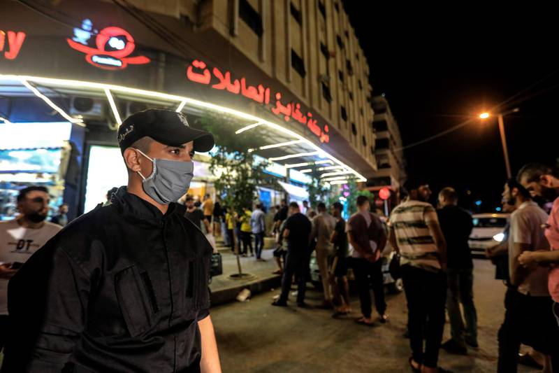A member of the Palestinian security forces monitors shoppers queuing for bread after the announcement of restrictions in the Gaza City amid rising numbers of coronavirus cases.  AFP