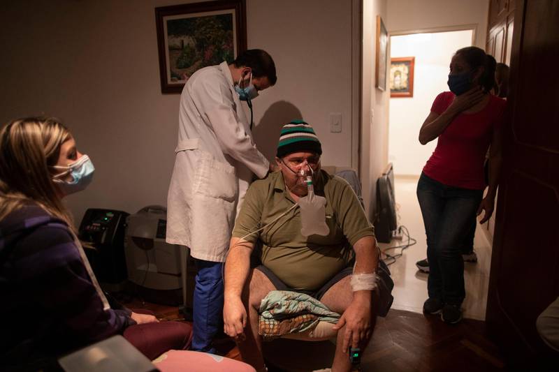 Doctor Leonardo Acosta, left, listens to the lungs of Carlos Perez, a Covid-19 patient, at his home in Caracas, Venezuela. AP Photo
