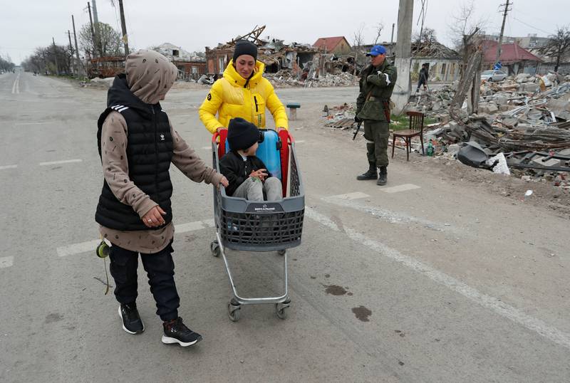 Local residents push a cart with a child past destroyed buildings in Mariupol. Reuters