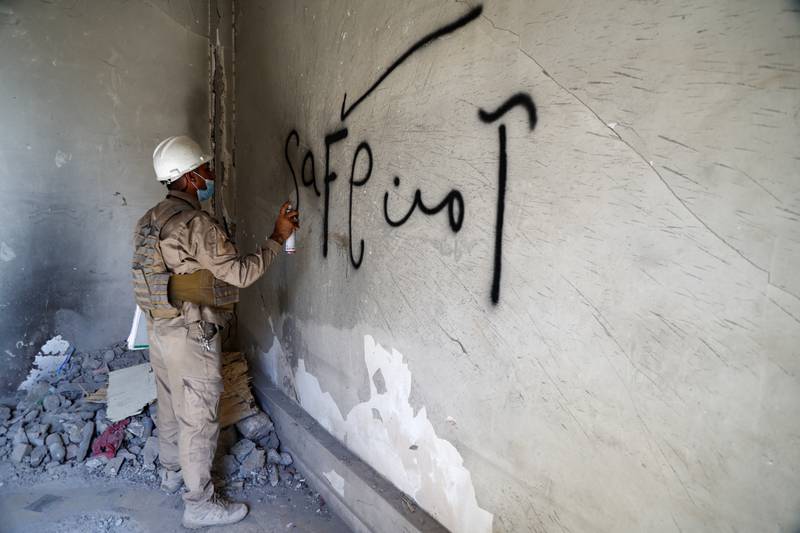 A member of a demining squad writes the word 'safe' on a wall.