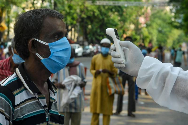 A man gets his body temperature checked as he queues to receive relief material during a lockdown in Kolkata.  AFP