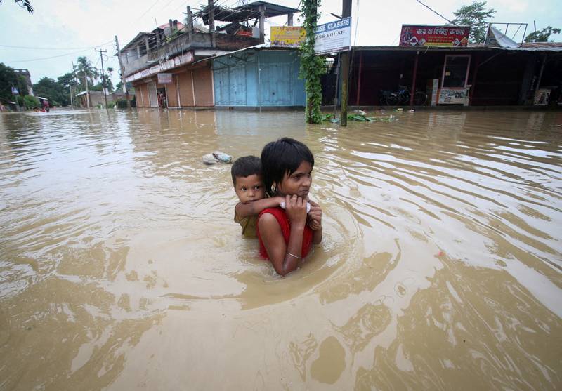 A girl carries her brother as she wades through a flooded road after heavy rains on the outskirts of Agartala, India, June 18, 2022.  Reuters