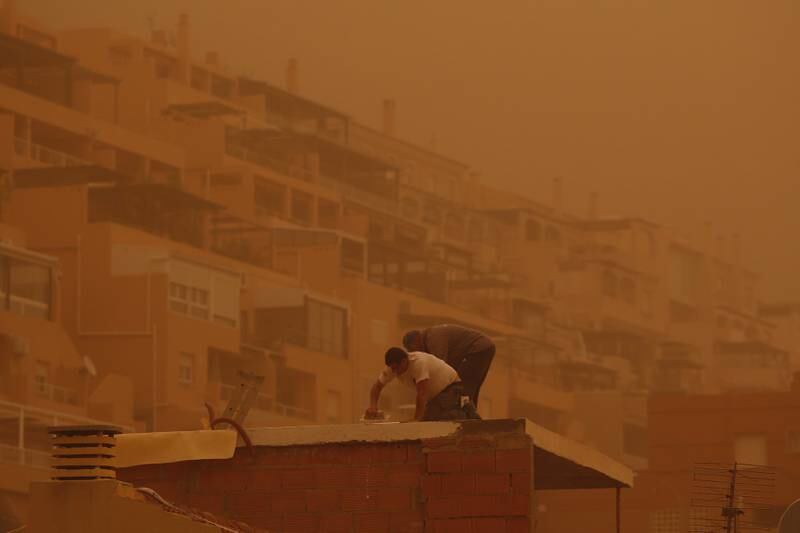 Two men work on the roof of a building as dust from the Sahara desert blankets the coastal city of Roquetas de Mar, Spain. EPA