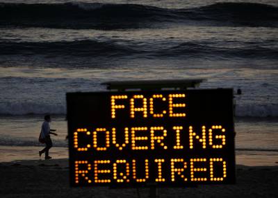 A woman feeding birds wears a mask as she walks along the beach during the coronavirus outbreak in Oceanside, California, US. Reuters