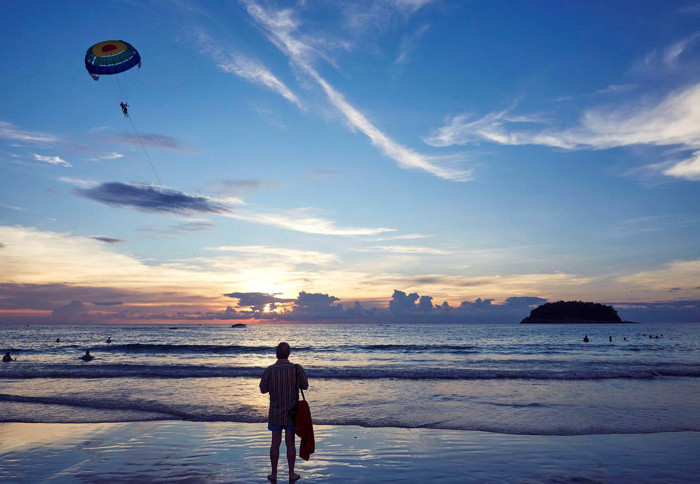 KATA BEACH, PHUKET, THAILAND - 2017/11/21: A beachgoer watches parasailing off the beach in Phuket. Tourists can take short parasailing flights from the beach out toward the small island, Koh Pu, and back again.  Phuket attracts more than 5 million tourists each year who flock there for it's picturesque beaches. (Photo by Craig Ferguson/LightRocket via Getty Images)