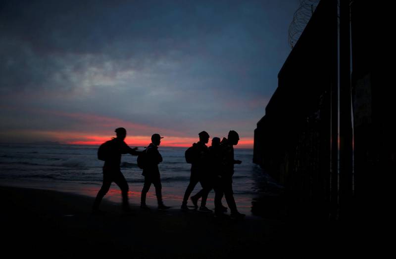 Migrants from Honduras, part of a caravan of thousands from Central America trying to reach the United States, walk next to the border fence as they prepare to cross it illegally, in Tijuana, Mexico. Reuters