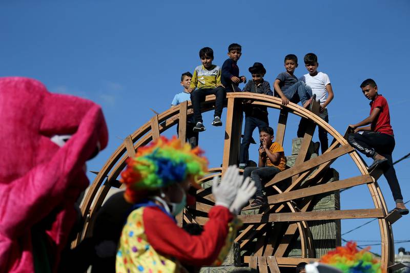 Children watch as a clown and men wearing costumes ride in a classic car to entertain Palestinians in the southern Gaza Strip. Reuters