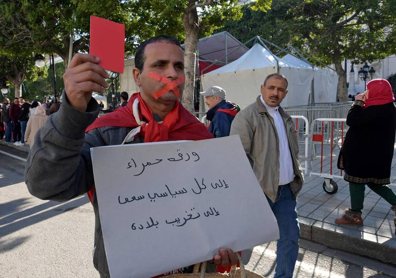 A Tunisian protester holds a red card as he holds a placard with a slogan criticising politicians in his country during a rally marking the ninth anniversary of the 2011 uprising, at Habib Bourguiba Avenue in Tunis on January 14, 2020. AFP