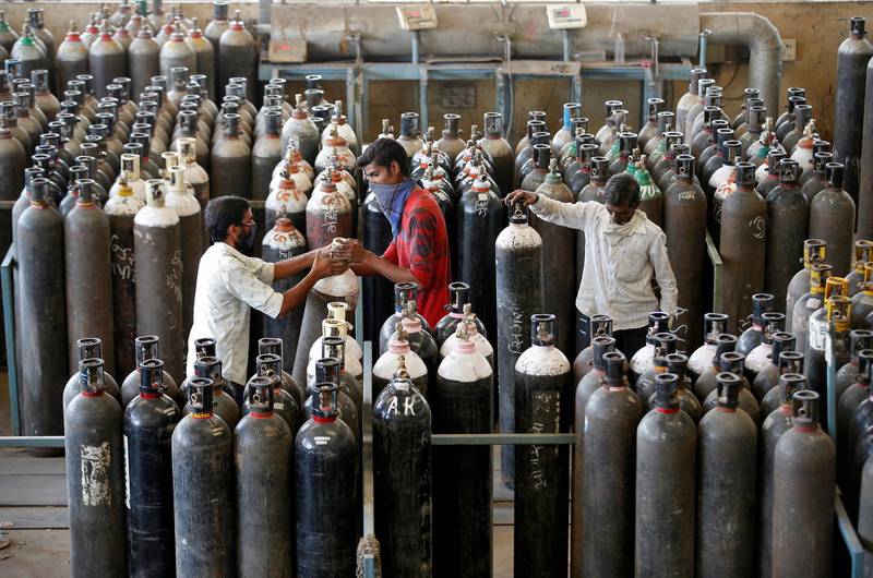 People carry oxygen cylinders after refilling them at a factory amid a surge in coronavirus cases in India's western city of Ahmedabad. Reuters