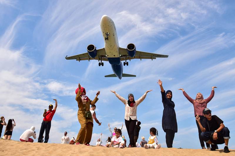 Tourists pose for picture on Mai Khao Beach as a plane lands at Phuket Airport in Thailand. AFP