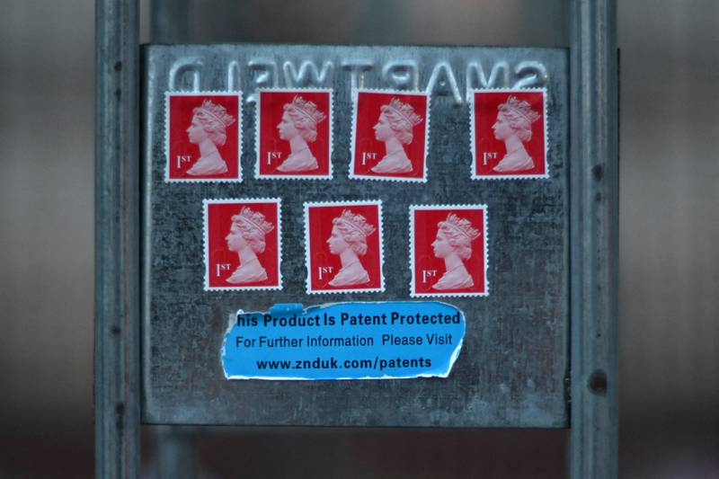 A tribute in the form of 1st class stamps bearing the image of Queen Elizabeth II is pictured stuck to railings outside of Buckingham Palace in London. Stamps, coins and passports will now change to show King Charles III. AFP