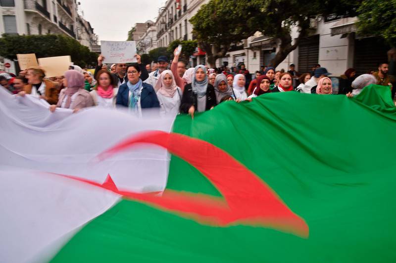 TOPSHOT - Algerians carry a giant national flag as they take part in a demonstration in the capital Algiers against President Abdelaziz Bouteflika on March 19, 2019.  Bouteflika today confirmed he will stay in power beyond his term expiring next month, despite tens of thousands of people demonstrating against his rule. / AFP / RYAD KRAMDI                        
