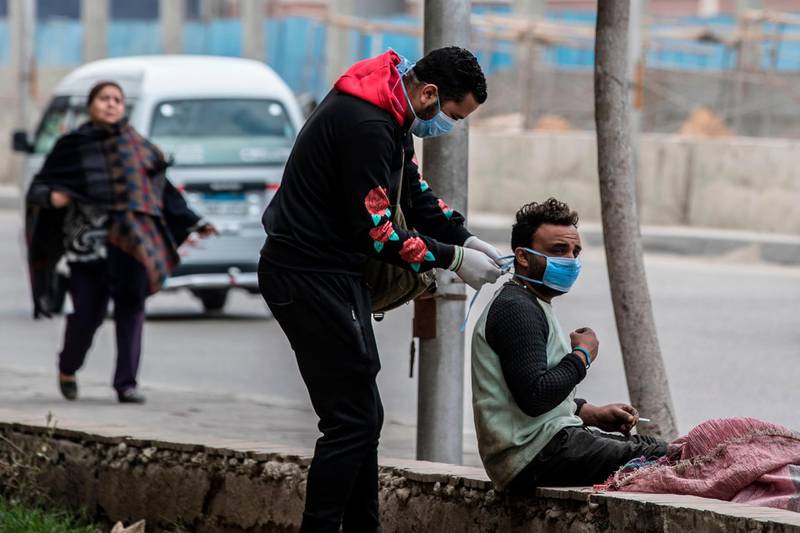 An volunteer ties a mask onto an Egyptian man in a street in Cairo. AFP
