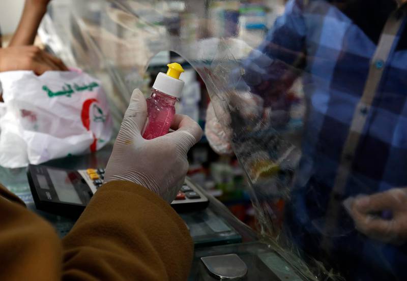 A customer wearing protective gloves buys sterilizing gel through a plastic shield installed as a precautionary measure against the spread of the coronavirus at a pharmacy in Sanaa, Yemen, on May 19, 2020. EPA