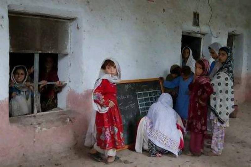 Girl students stand around teacher Rukhmina Abdul Rahman as she writes a daily timetable on a blackboard on the second day of a new school term at the BEFARe School #103 in Khattak Pul in the Shamshatoo Refugee Camp. Photo by Rebecca Conway