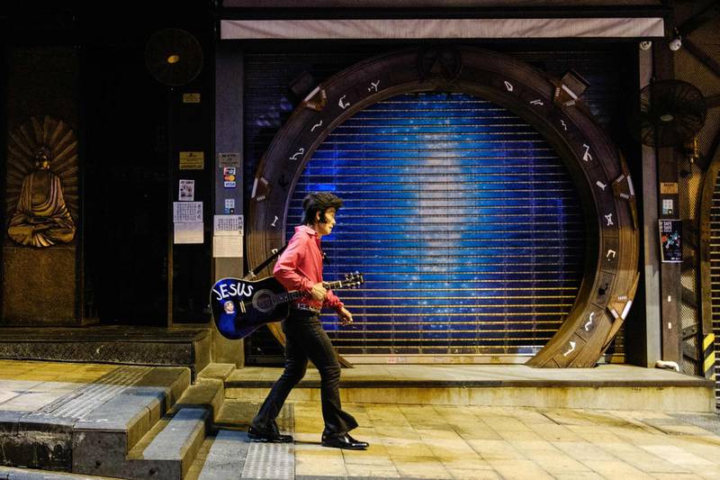 This photo taken on March 23, 2020 shows Kwok Lam-sang, 67, who has been performing covers of Elvis Presley songs under the name of "Melvis" since 1992, walking with his guitar past closed bars in the usually busy drinking area of Lan Kwai Fong in Hong Kong, after restaurants and bars in the city were banned from selling alcohol as a preventive measure against the spread of the COVID-19 novel coronavirus. / AFP / Anthony WALLACE
