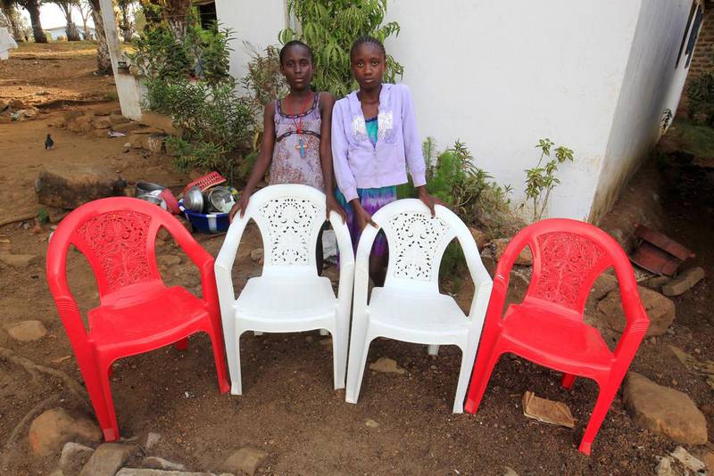 Sisters Diamond, right, and Secret Moore pose for a family portrait at their home in the Pipeline Community outside Monrovia, Liberia. The empty chairs represent their mother, father, grandmother and aunt who died of the Ebola virus during an outbreak of the disease in 2014. Ahmed Jallanzo / EPA