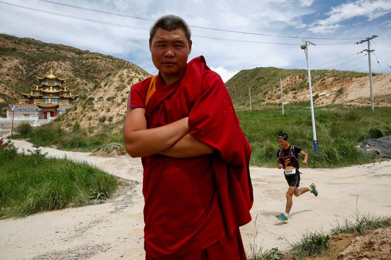 A Tibetan Buddhist monk talks to the photographer as a participants run past a temple during the Super Salmon ultra-marathon near the Longyangxia Reservoir in Gonghe County, Qinghai province, China, August 11, 2018.  Picture taken August 11, 2018.  REUTERS/Thomas Peter