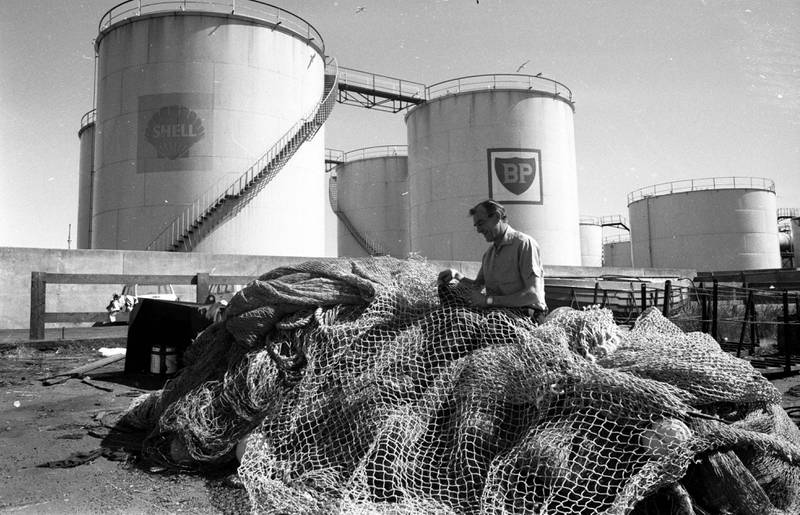 A fisherman attends to his nets beside oil storage containers on the coast at Aberdeen in 1975. Getty Images
