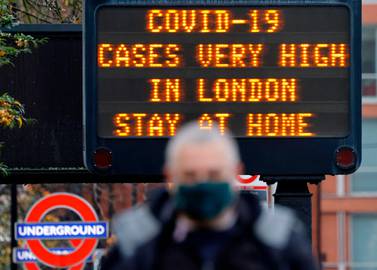 Pedestrians walk past a sign alerting people that "COVID-19 cases are very high in London - Stay at Home". AFP