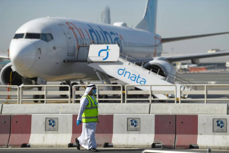 A mask-clad employee walks in front of a flydubai aircraft on the tarmac of Dubai International Airport.